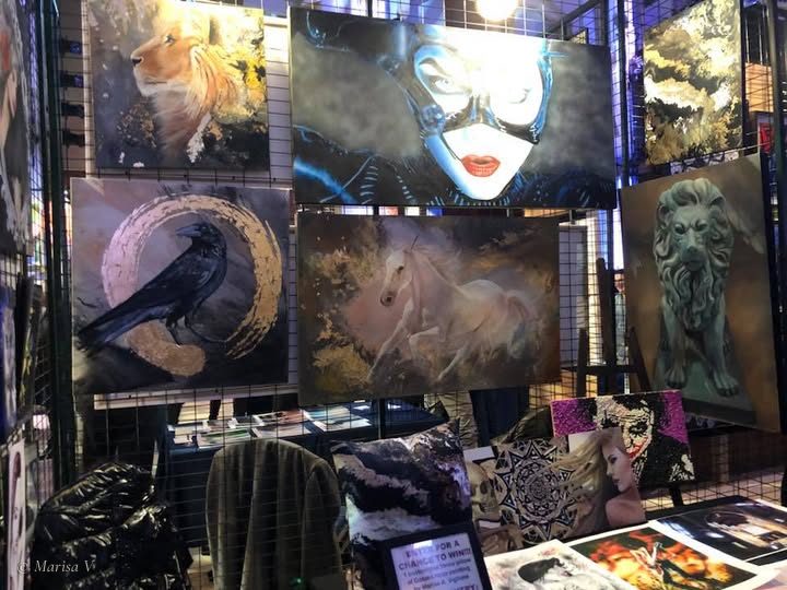 Le kiosque de Marisa V à MTL Uncovered, en 2018 : ses toiles accrochées sur des grilles noires, dont un corbeau dans un cercle d’or, un lion et un cheval blanc.