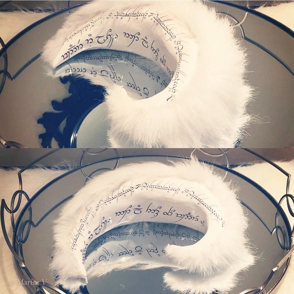 White crescent-shaped ceramic sculpture covered in calligraphic script and edged with white fur.