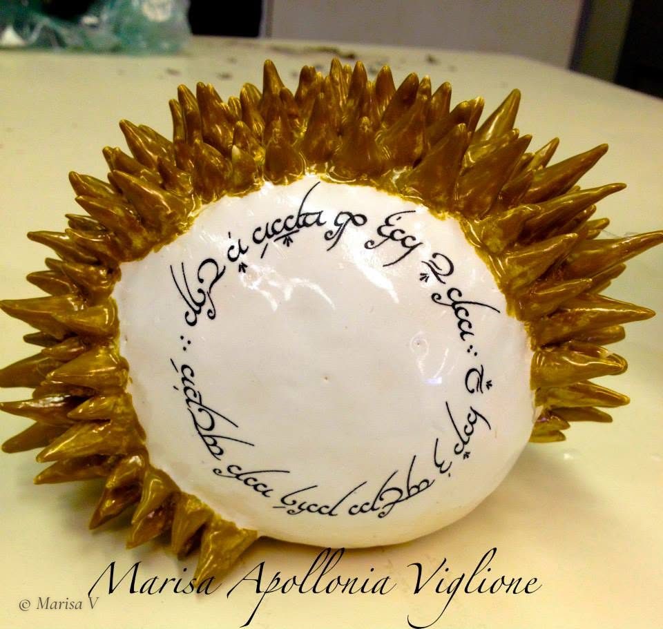 Ceramic sculpture bristling with gold spikes, its white face bearing a circular inscription in Elvish script.