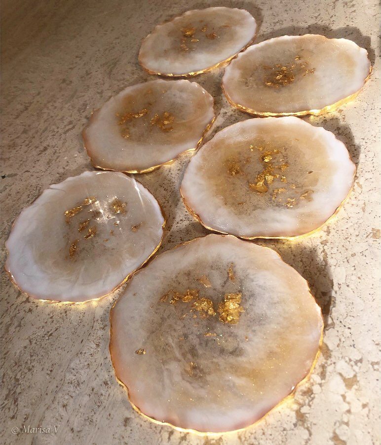 Six irregular round coasters in ivory resin, with flakes of gold leaf at the centre and a gilded rim.