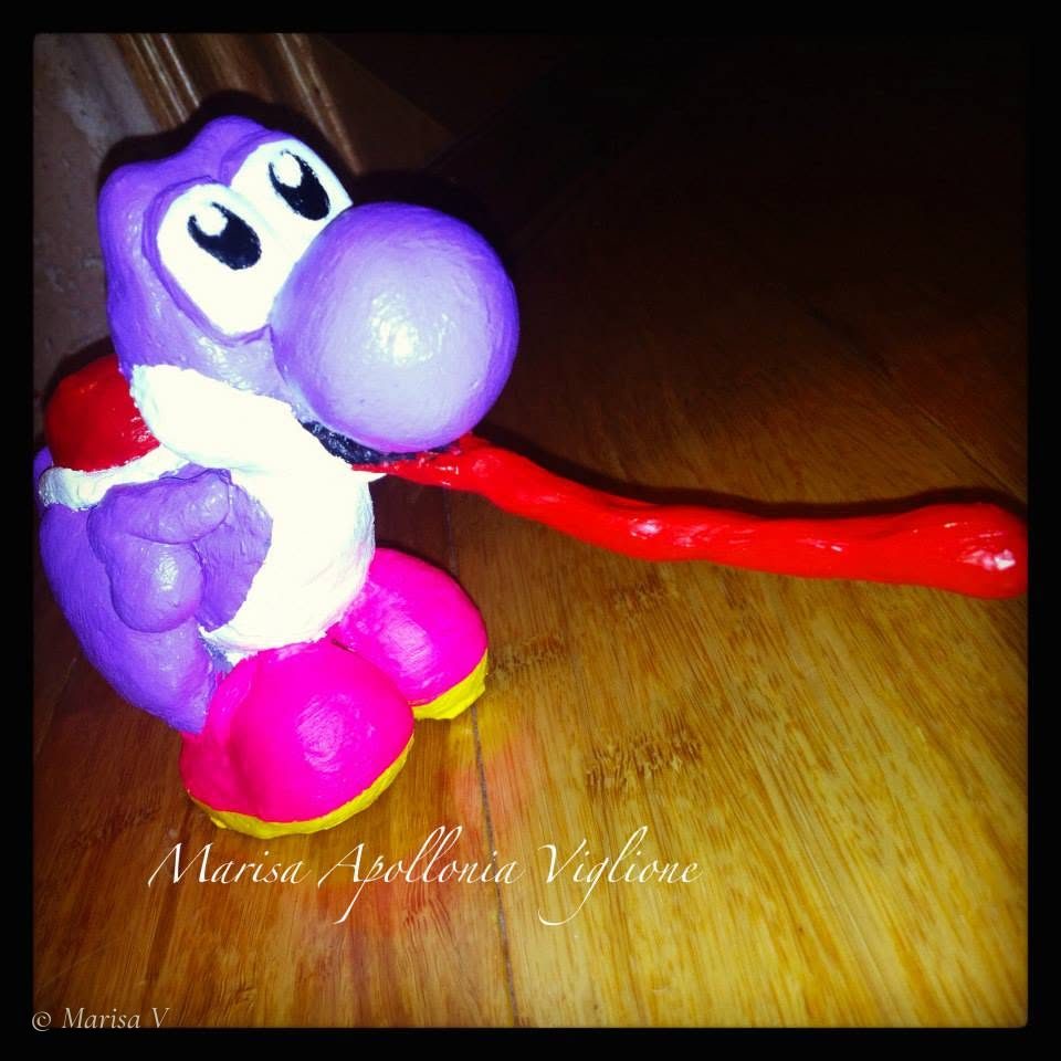Painted clay figurine of a purple Yoshi with its red tongue unrolled, on a wooden floor.